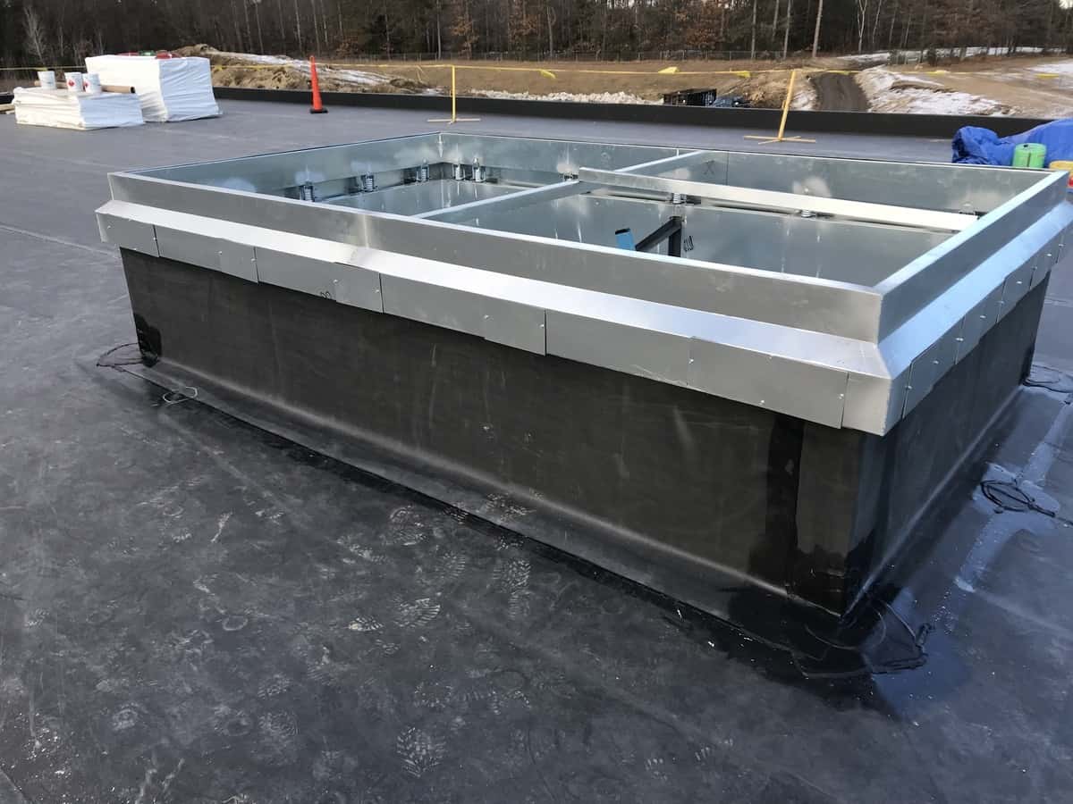 Rubber-Roofing-by-Twin-Metals-008 Rubber roofing installation with a silver metal edge, showcasing a flat roof structure, surrounded by construction materials and equipment, relevant to Twin Roofing's high-quality roofing services for residential and commercial properties.