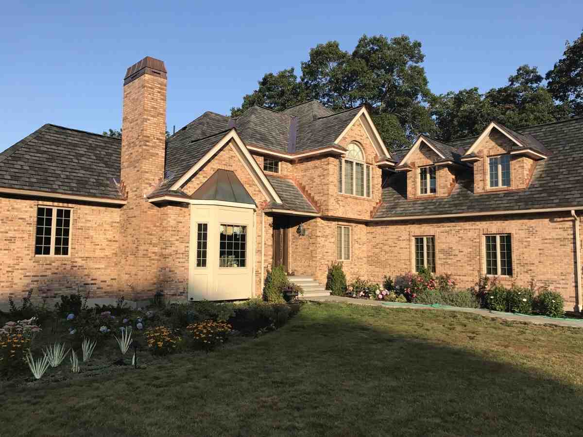 Residential home with new architectural shingle roofing, brick exterior, and landscaped garden, showcasing Twin Roofing's quality craftsmanship and design.